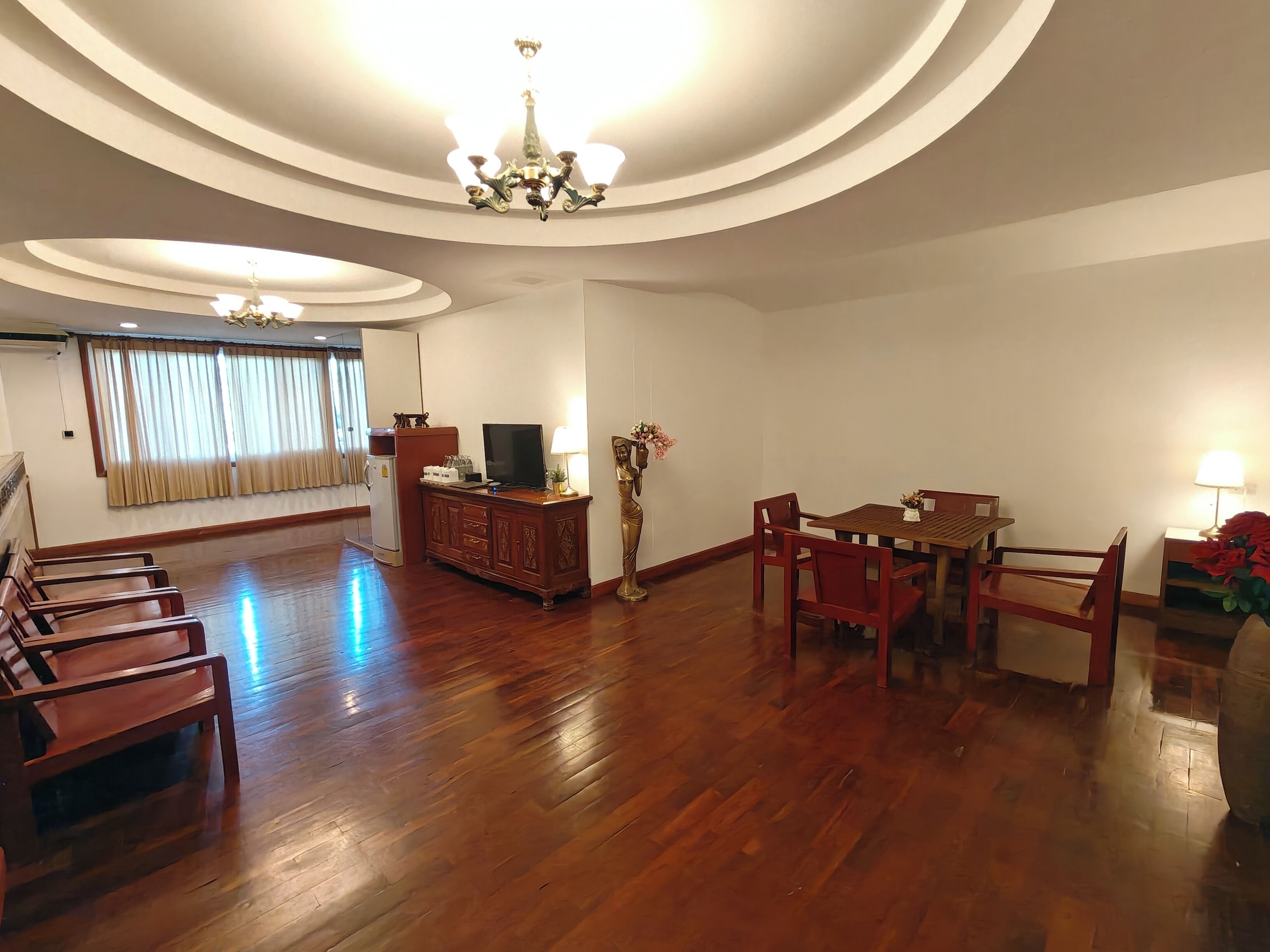 Un salón comedor espacioso con suelo de madera, una mesa y sillas, un televisor sobre un mueble bajo y una araña.