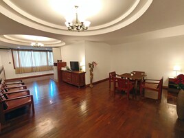 Un salón comedor espacioso con suelo de madera, una mesa y sillas, un televisor sobre un mueble bajo y una araña.