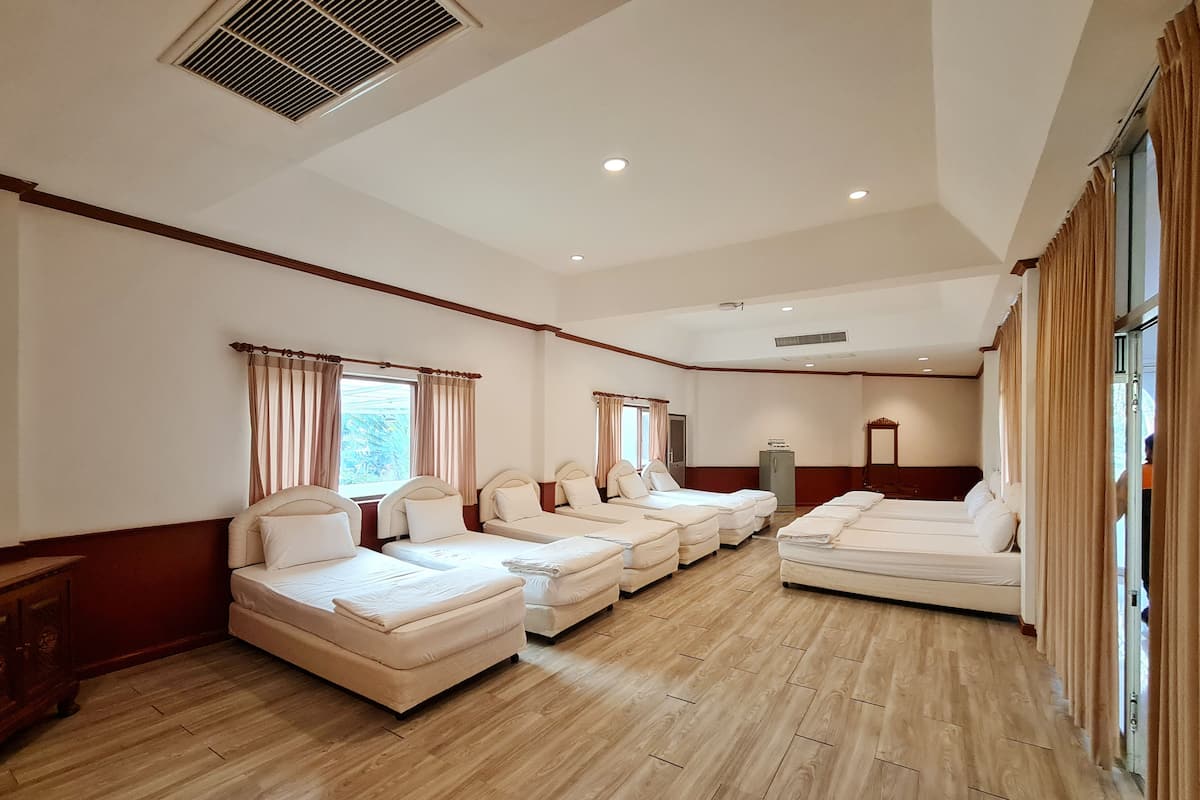 A hotel room with multiple beds arranged in a row, wooden flooring, and large windows with curtains.