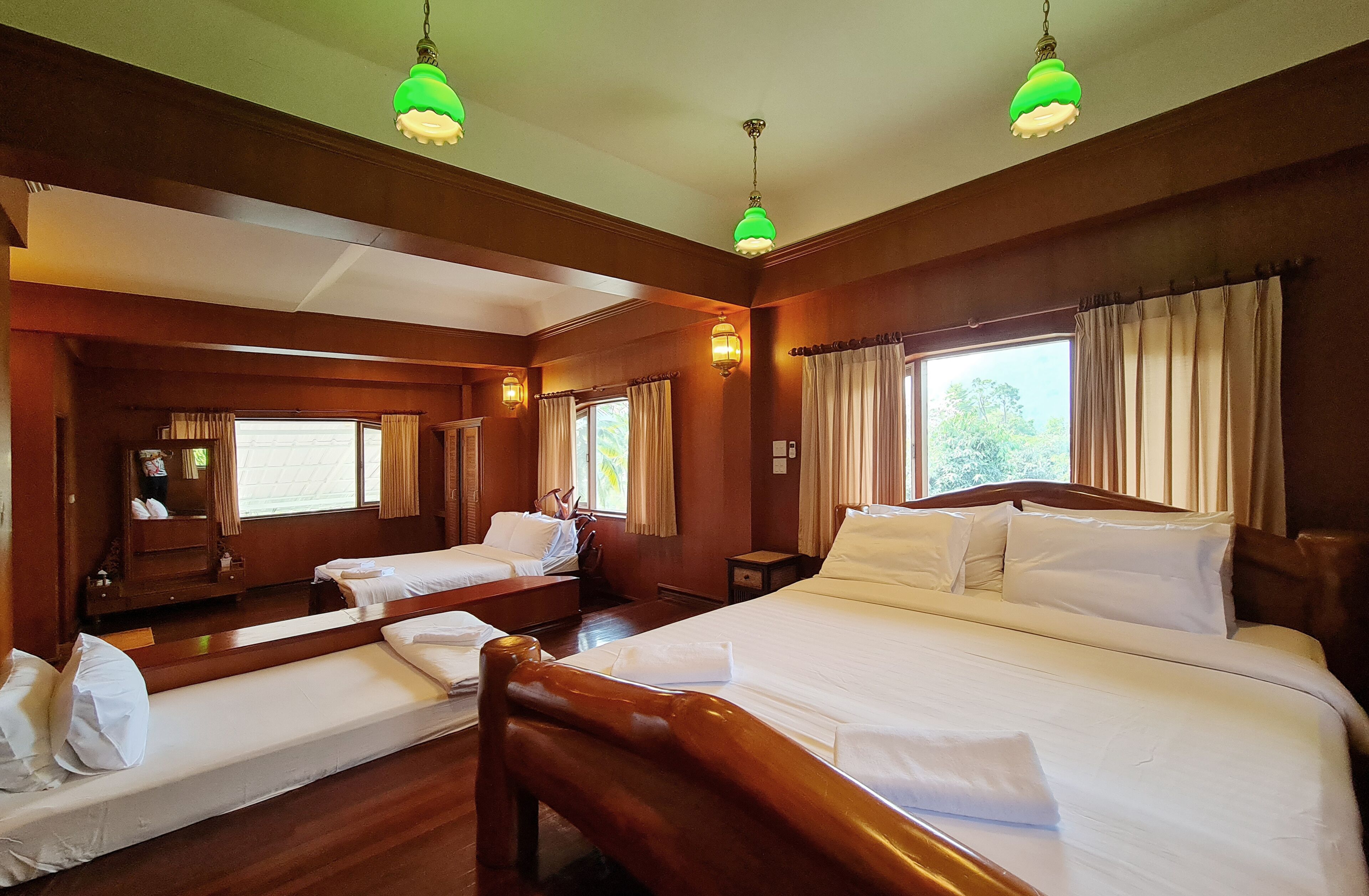 A hotel room with a large bed, two smaller beds, wooden headboards, and green pendant lights.