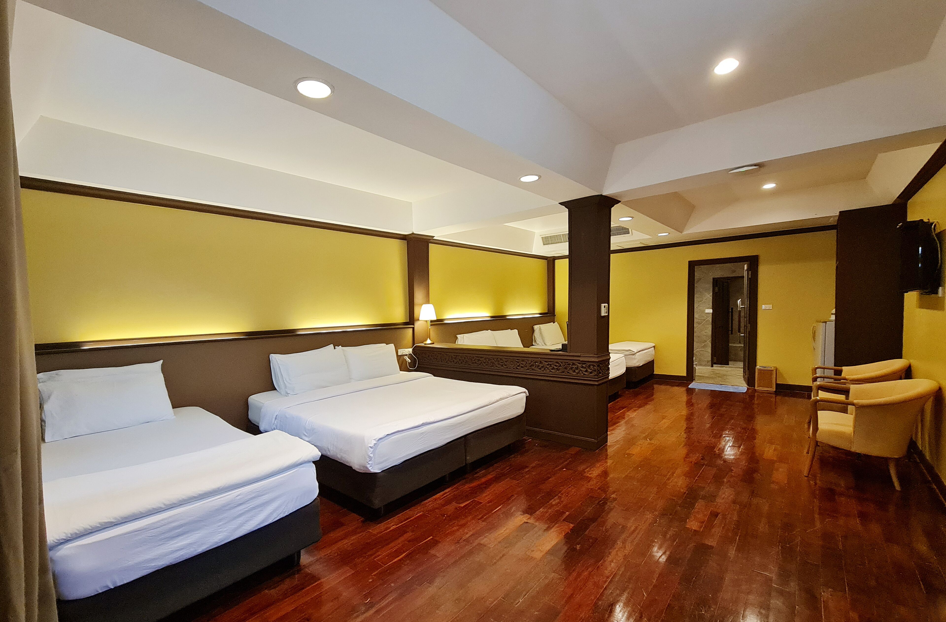 A hotel room with two beds, a wooden floor, a mirror, and a television.