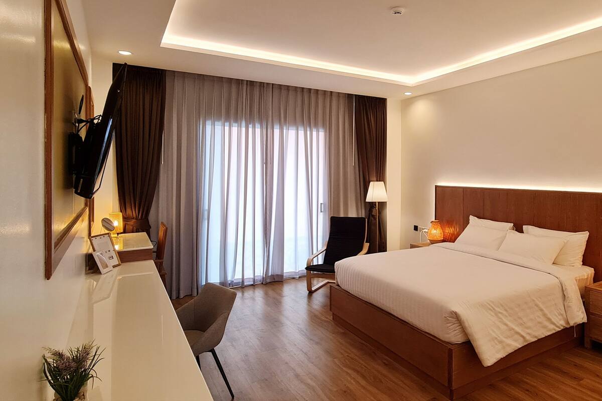 A modern hotel room with a large bed, bedside lamps, a desk with a chair, and a TV mounted on the wall.