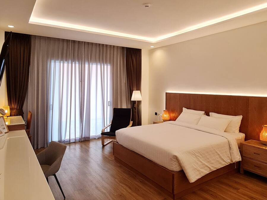 Una habitación de hotel moderna con una cama grande, lámparas de noche, un escritorio con silla y un televisor montado en la pared.