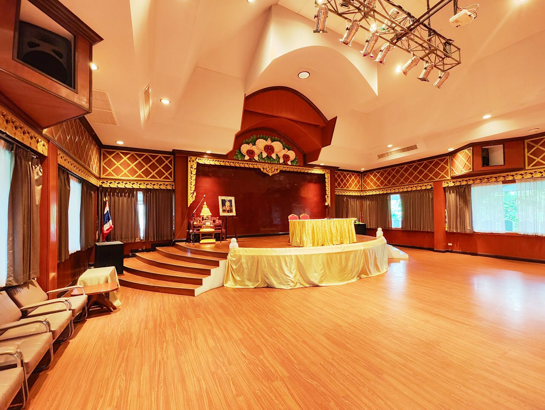 Un amplio salón con un escenario, un atril y una mesa cubierta con un mantel amarillo.