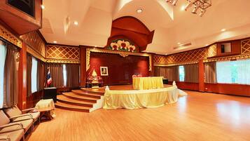 Un amplio salón con un escenario, un atril y una mesa cubierta con un mantel amarillo.