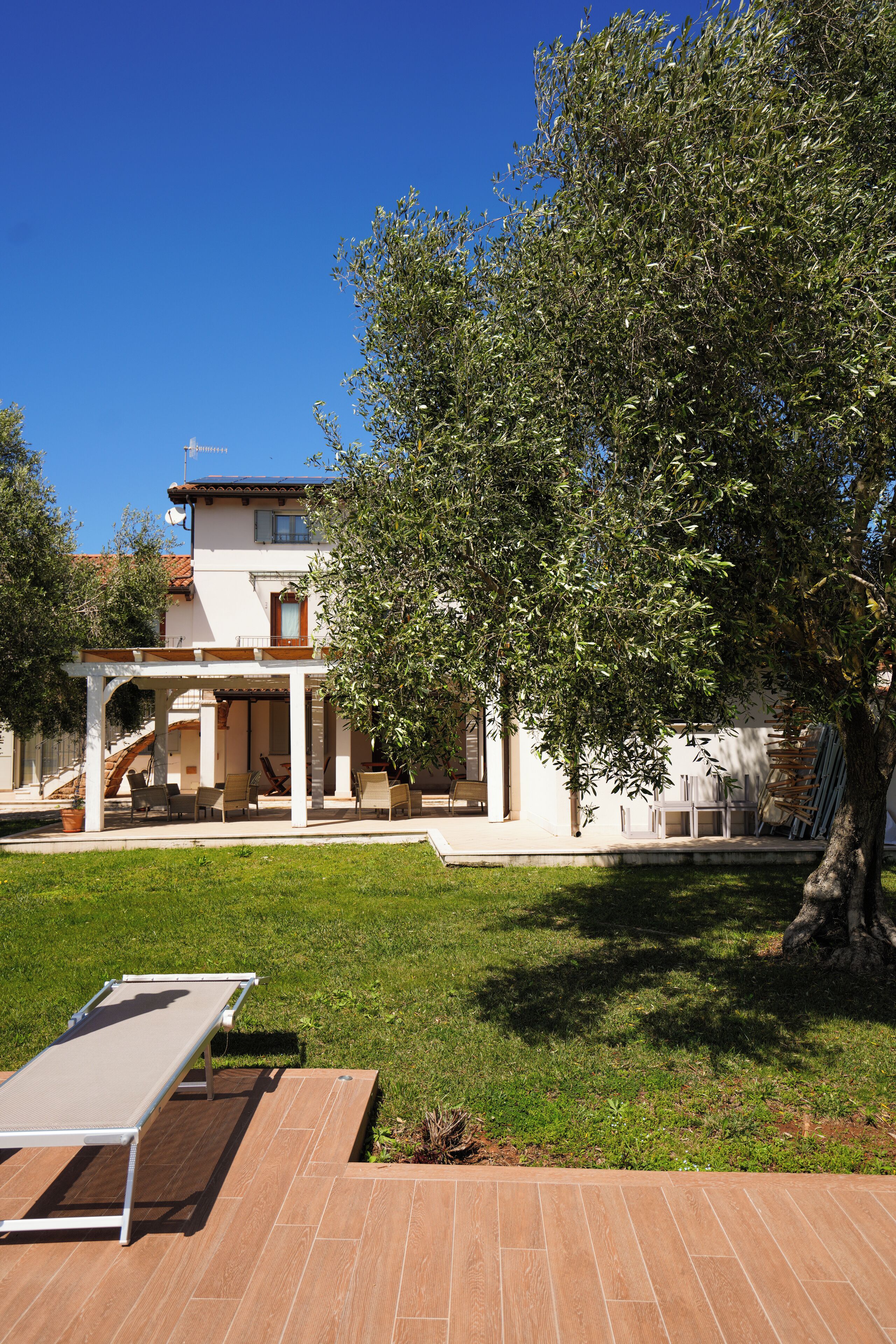 Una casa con un porche cubierto, césped y un árbol grande.