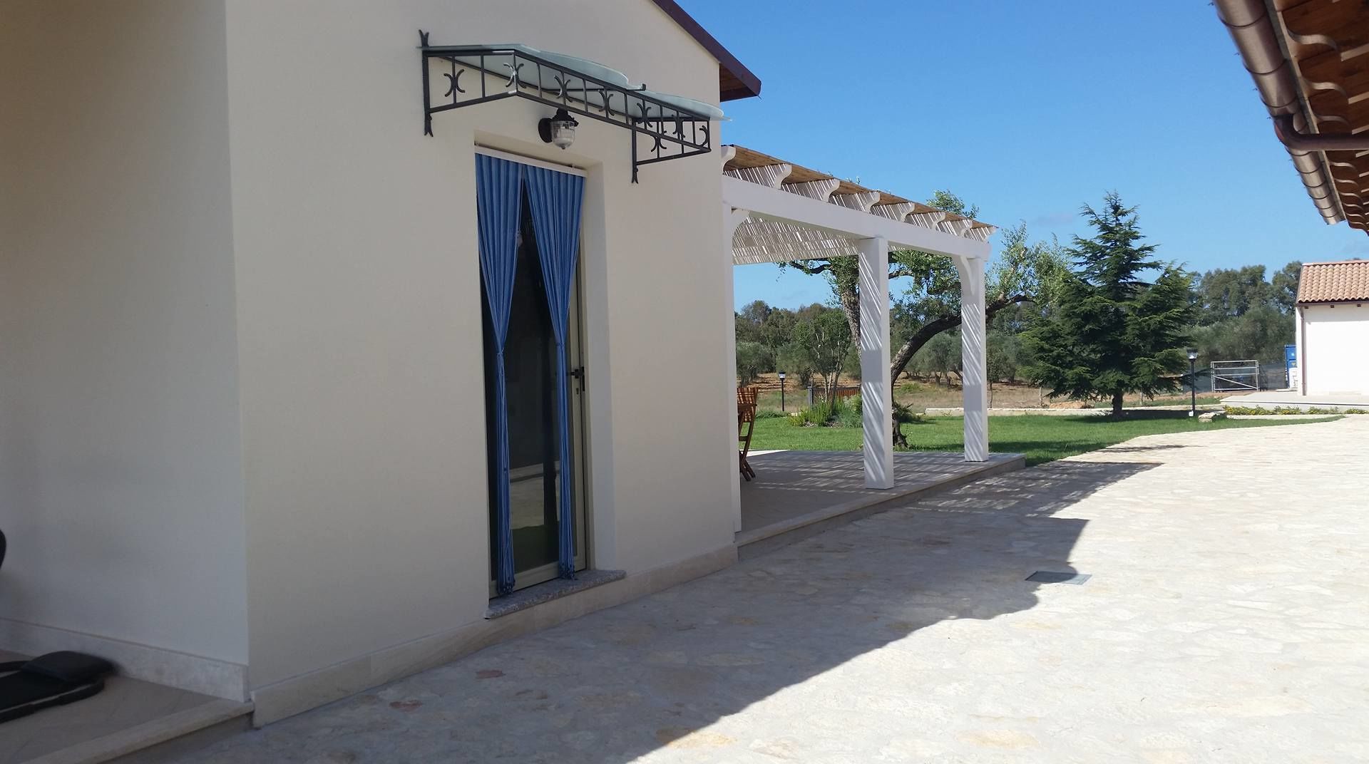 Een gebouw met een witte gevel, een blauwe deur en een overdekt buitengebied met een pergola.
