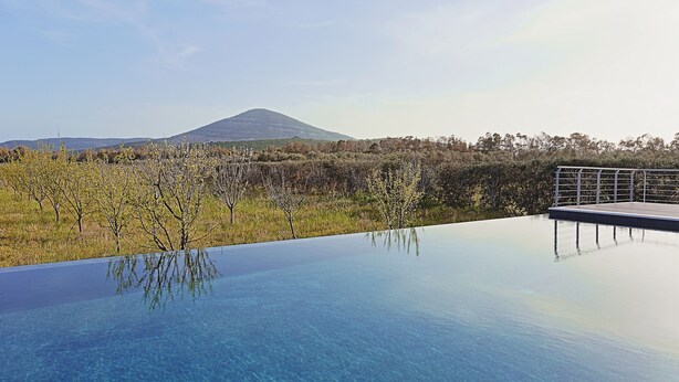 A clear pool with a view of a mountain and trees. - Agriturismo Casale degli Ulivi (Alghero)