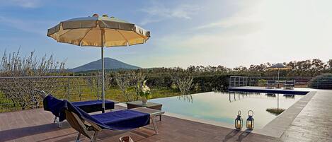 A poolside area with lounge chairs, a covered umbrella, and a view of a mountain.