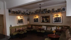 A cozy lounge area with a green sofa, round tables, and a patterned wall with framed pictures. - Abbey Grange Hotel (Nuneaton)