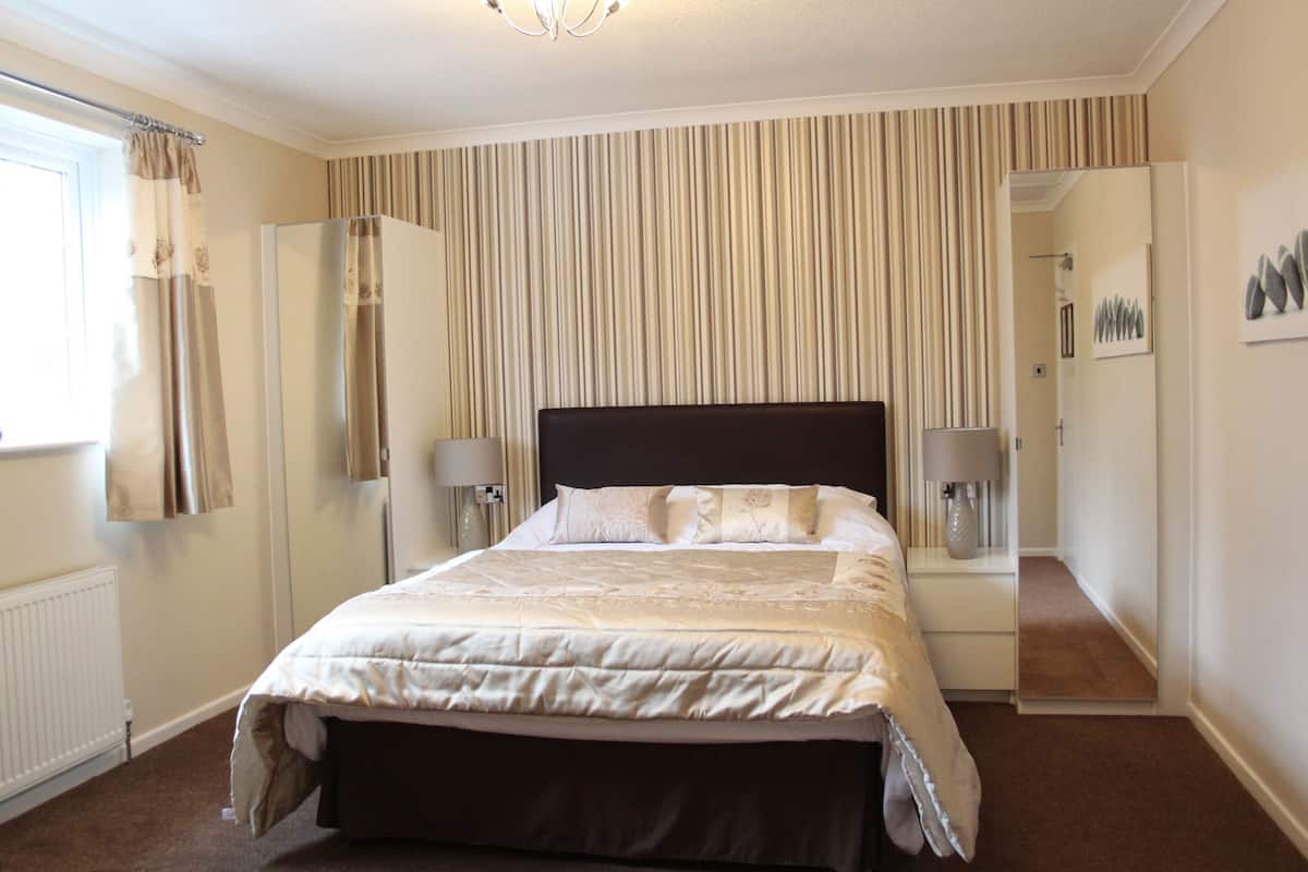 Een slaapkamer met een groot bed, een spiegel, een radiator en een raam met gordijnen.
