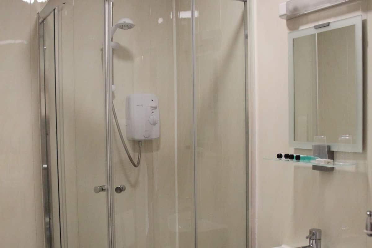 Een badkamer met een douche met glazen wand, een wit wastafelmeubel en een spiegel erboven.