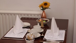 A dining table set with white napkins, plates, cutlery, and a menu. A small bowl with condiments and a sunflower in a copper vase are also visible. - Abbey Grange Hotel (Nuneaton)