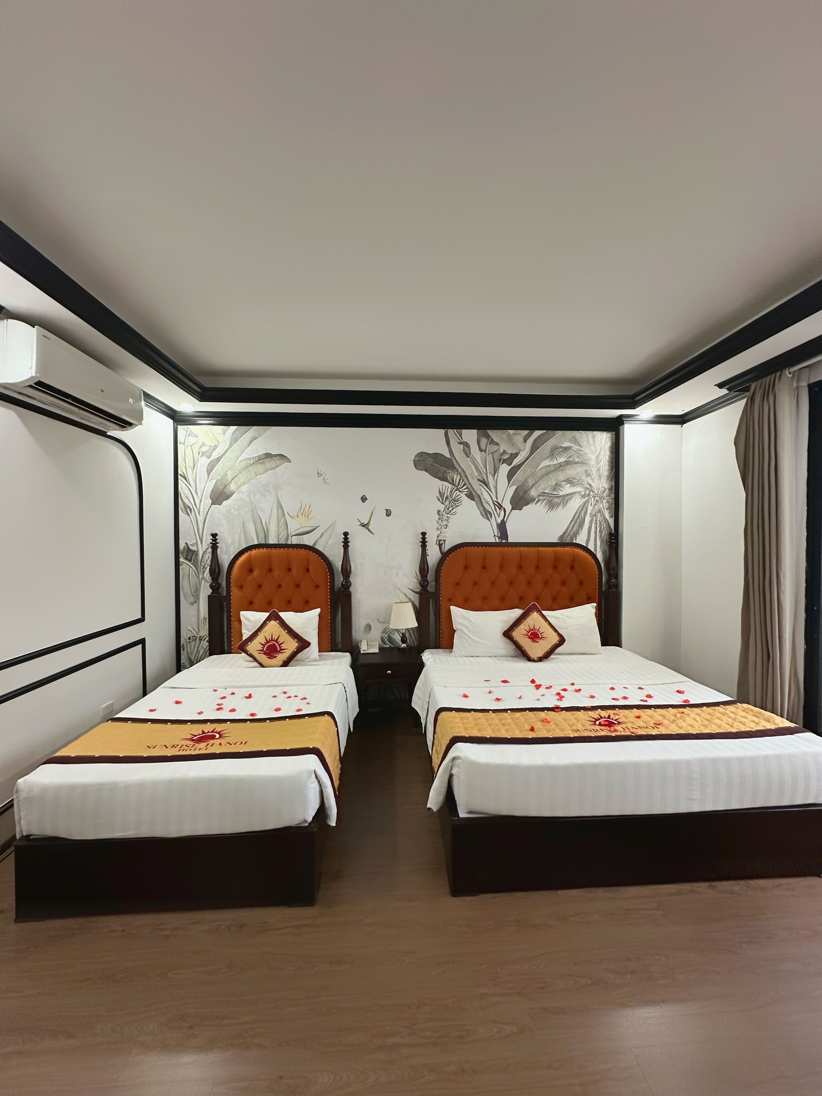 A hotel room with two beds, a wall mural, an air conditioning unit, and a wooden floor.