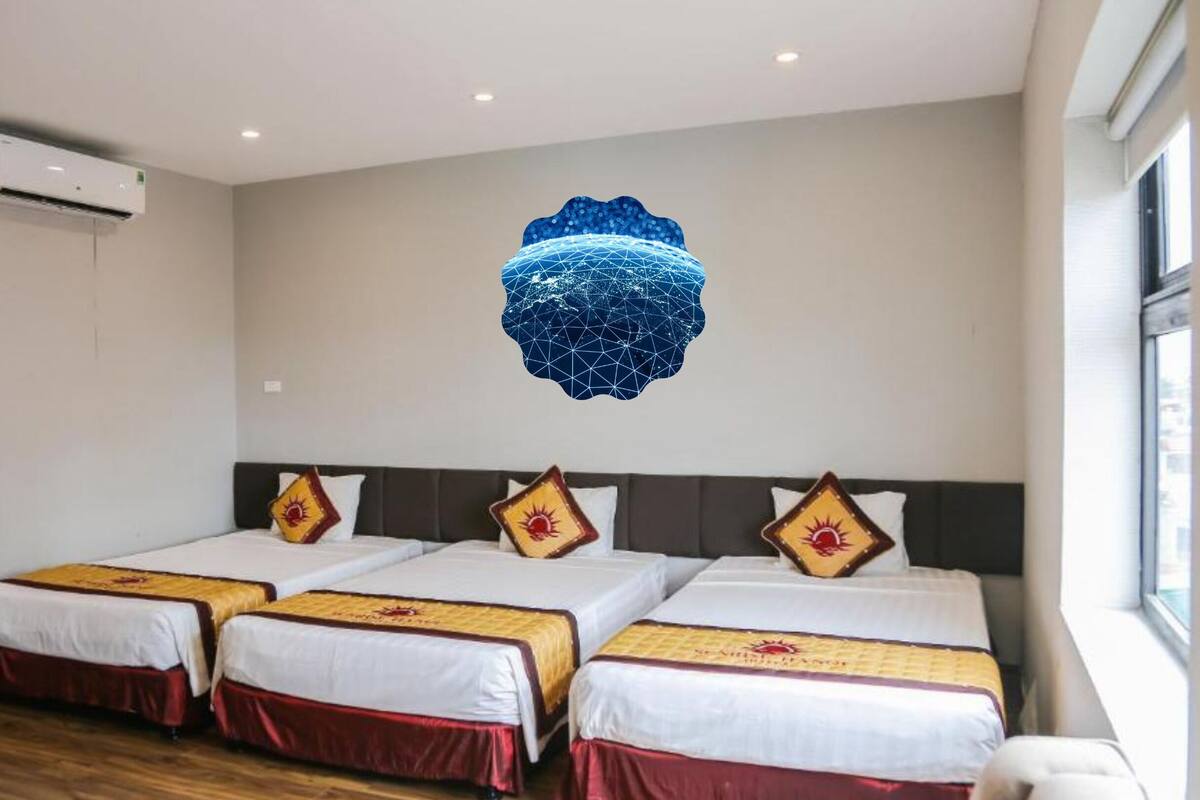 Et hotelværelse med tre senge, en fastmonteret aircondition og et stort vindue.