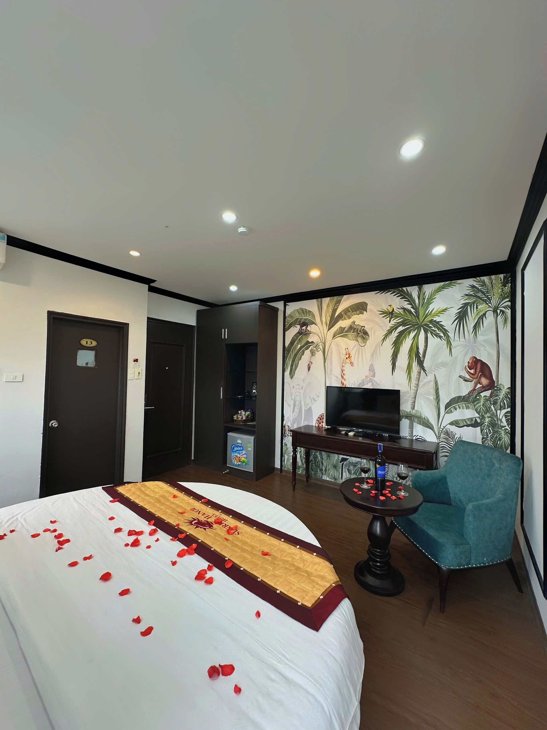 A hotel room with a bed, a TV, a small table with drinks, and a chair.