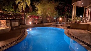 A swimming pool with a curved edge, surrounded by a stone border and a low wall. There are lounge chairs and a table with chairs on the right side. - 4 Bedroom Villa TG48 on beachfront resort SDV288-By Samui Dream Villas (Koh Samui)