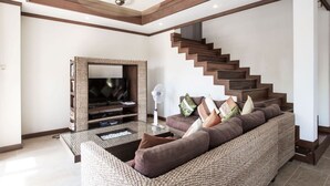 A modern living room with a large flat-screen TV, a comfortable sofa, a staircase, and a ceiling fan. - 4 Bedroom Villa TG48 on beachfront resort SDV288-By Samui Dream Villas (Koh Samui)