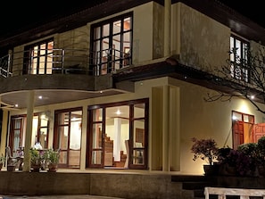 A two-story house with a balcony, large windows, and potted plants.