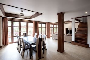 A spacious dining area with a large table and chairs, large windows with curtains, a staircase, and a cozy seating area.