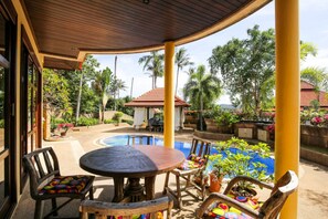 Ein Außenbereich mit Terrasse, Pool, Holzmöbeln und tropischen Pflanzen.