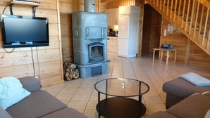 Un interior de cabaña acogedor, con chimenea de piedra, paredes de madera y un televisor de pantalla plana montado en la pared.