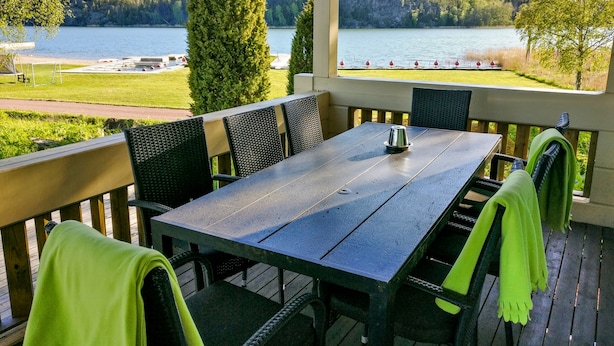 Un espacio comedor al aire libre techado, con una mesa y sillas, con vistas a un lago y colinas boscosas.