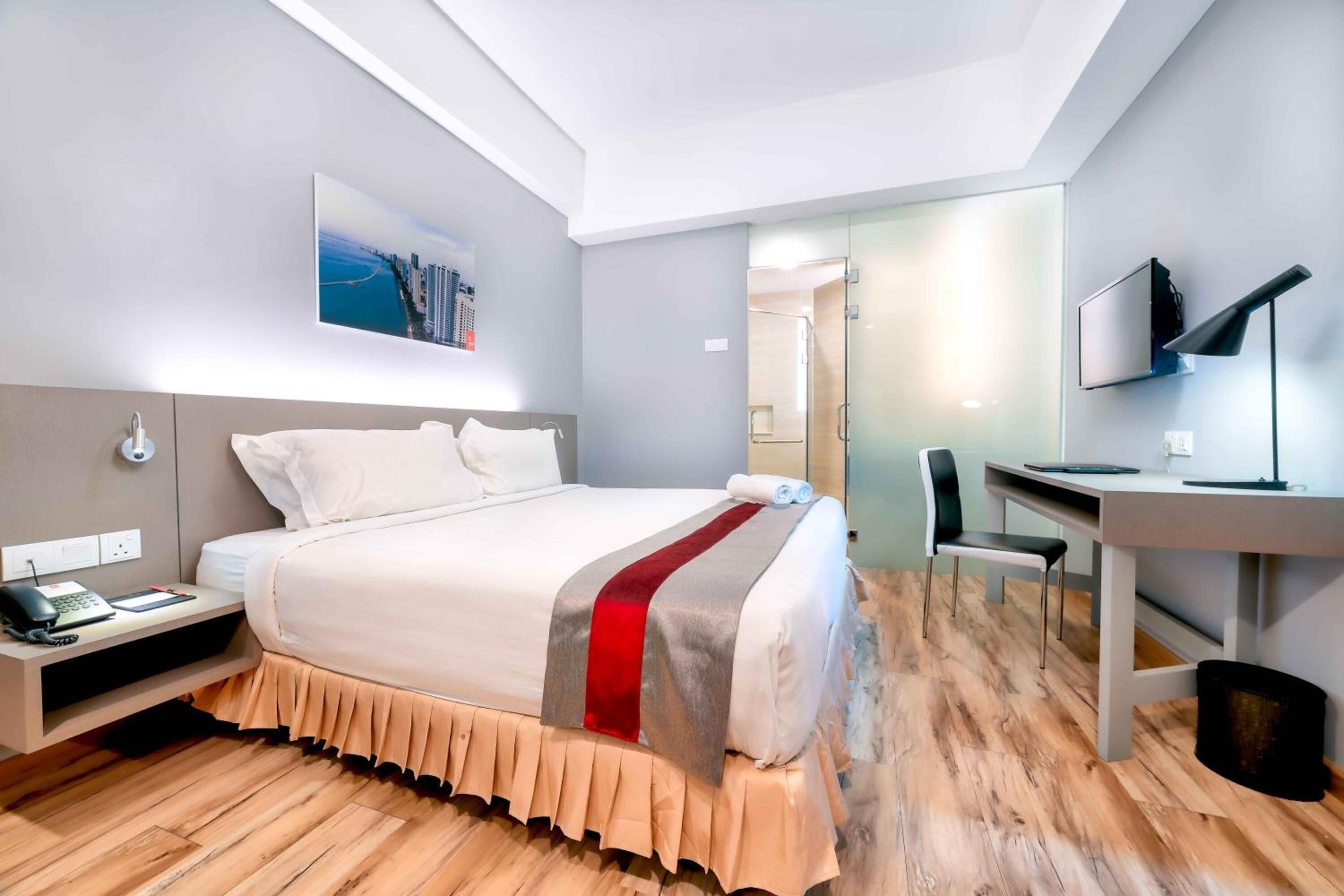 A modern hotel room with a large bed, a desk, and a television.