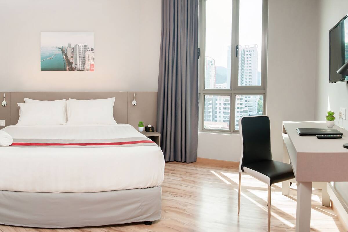 A hotel room with a bed, a desk, a chair, a TV, and a window with a city view.