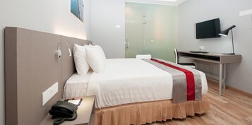 Una habitación de hotel moderna con cama, mesita de noche, teléfono, televisor y un escritorio con silla.