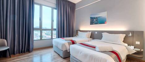 A hotel room with two beds, a large window with curtains, a painting on the wall, and a bedside table with a lamp.