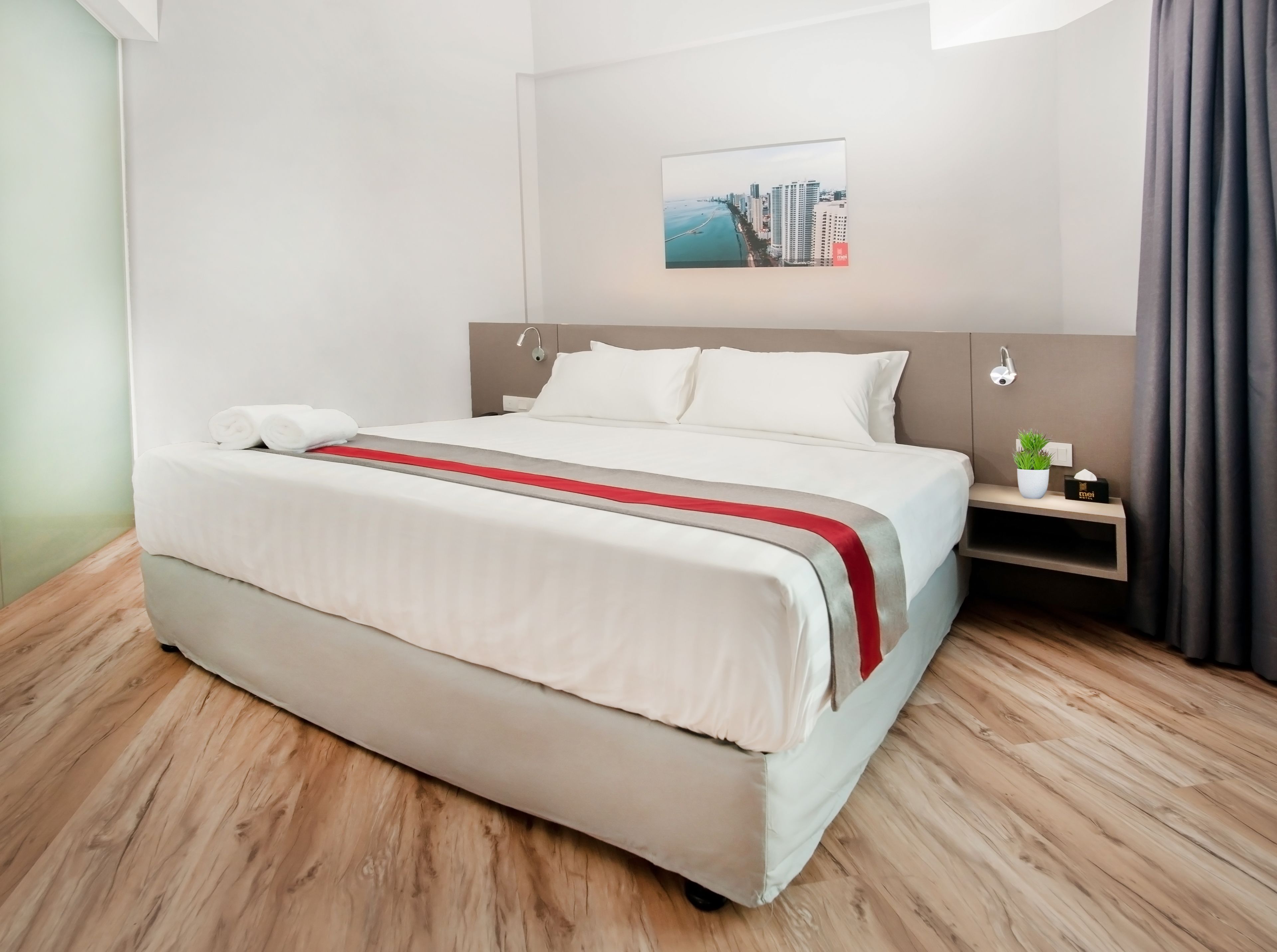 A neatly made bed with a red and white bedspread, a headboard, and a nightstand with a plant and a tissue box.