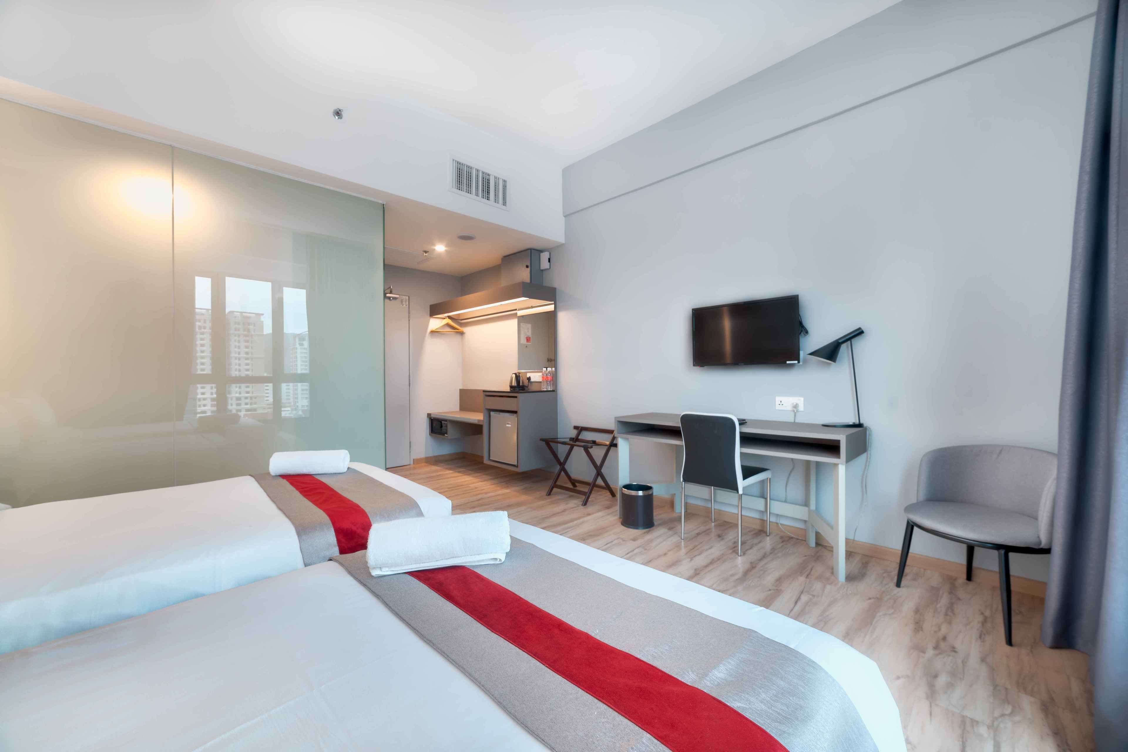 A modern hotel room with two beds, a desk, a chair, a TV, and a small kitchenette.