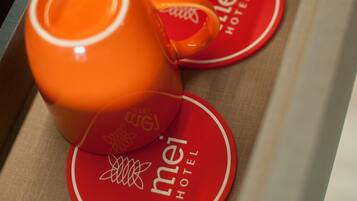 Un cajón con tres tazas naranjas y dos posavasos rojos con la marca del hotel.