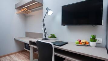 A modern office space with a desk, chair, lamp, television, and a small plant on the desk.