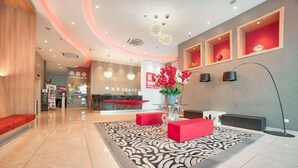Eine Hotelhalle mit Empfangstresen, roten Sitzmöglichkeiten, einem gemusterten Teppich und dekorativen Wandregalen.