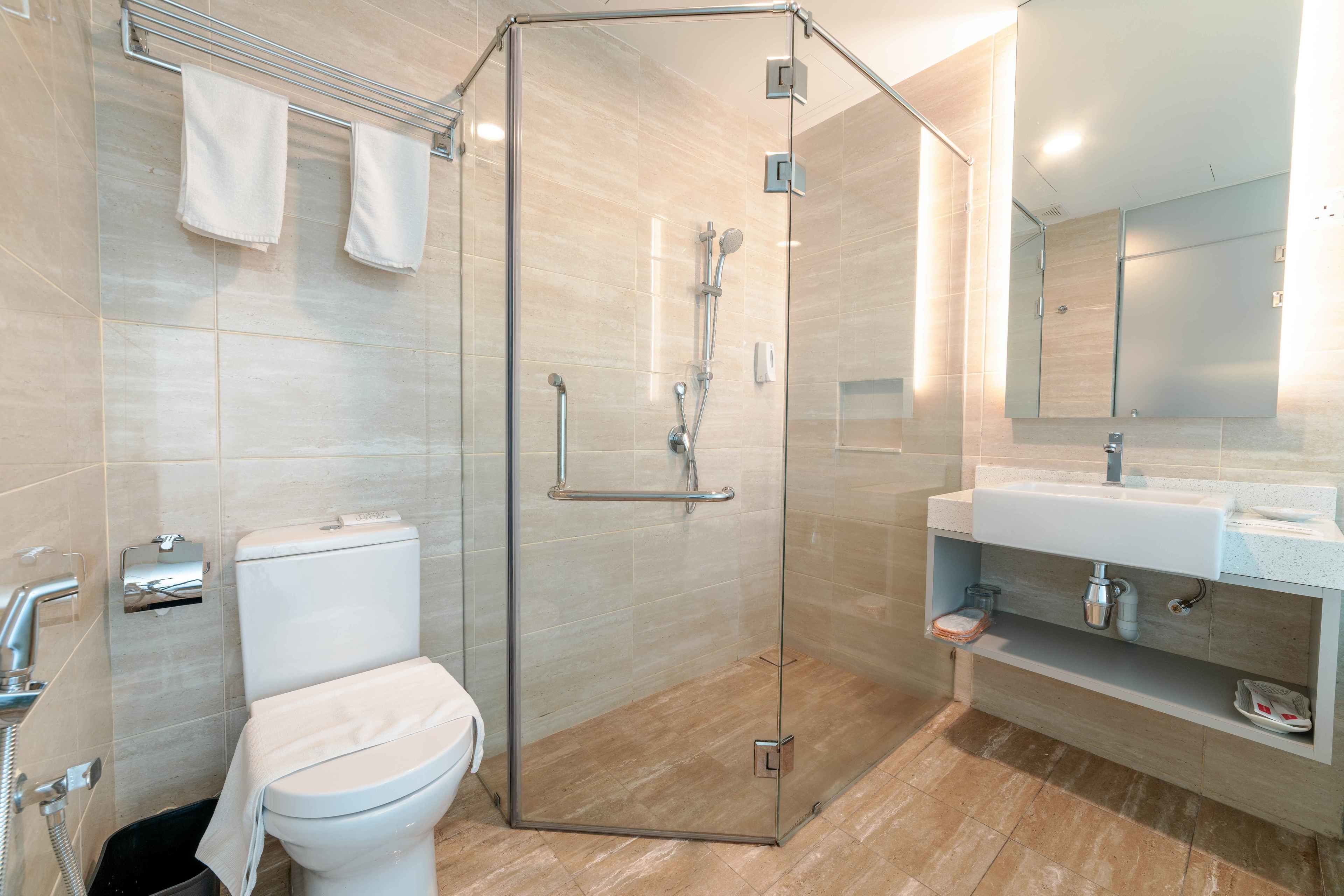 A modern bathroom with a glass-enclosed shower, a toilet, and a sink with a mirror above it.