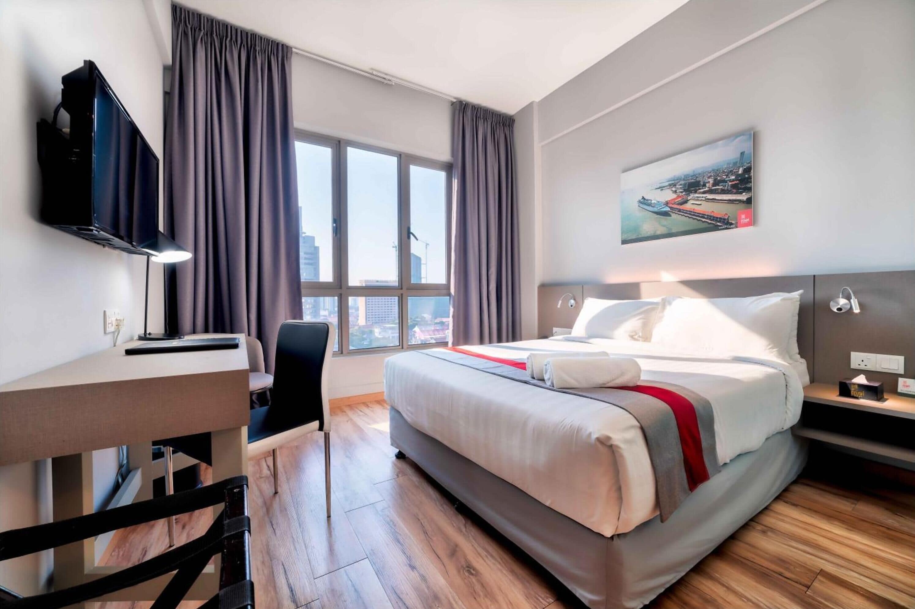 A hotel room with a bed, a desk, a chair, a TV, and a window with curtains.