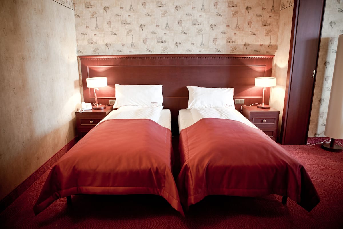 A double bed with two bedside tables, each with a lamp, in a room with patterned wallpaper and a wooden headboard.