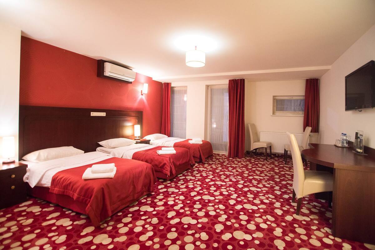 A hotel room with two beds, a desk, a chair, and a television.