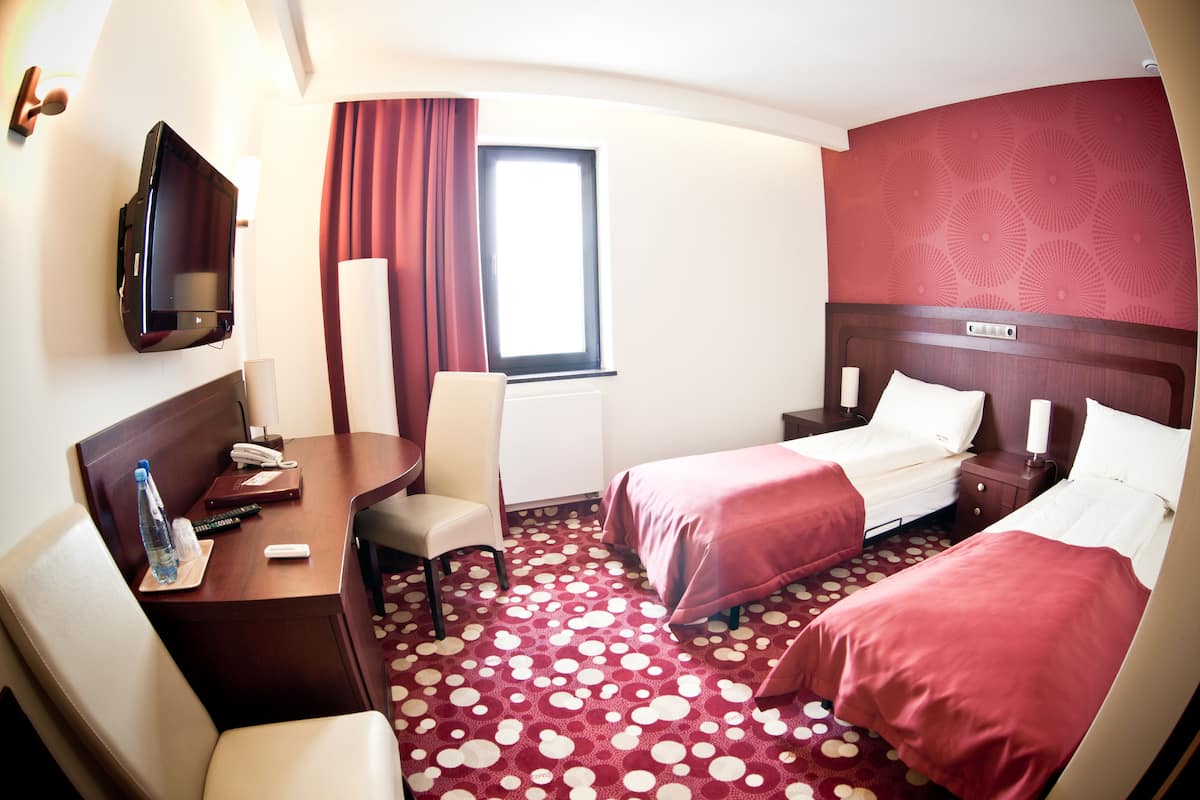 A hotel room with two beds, a desk with a chair, a TV, and a window with curtains.