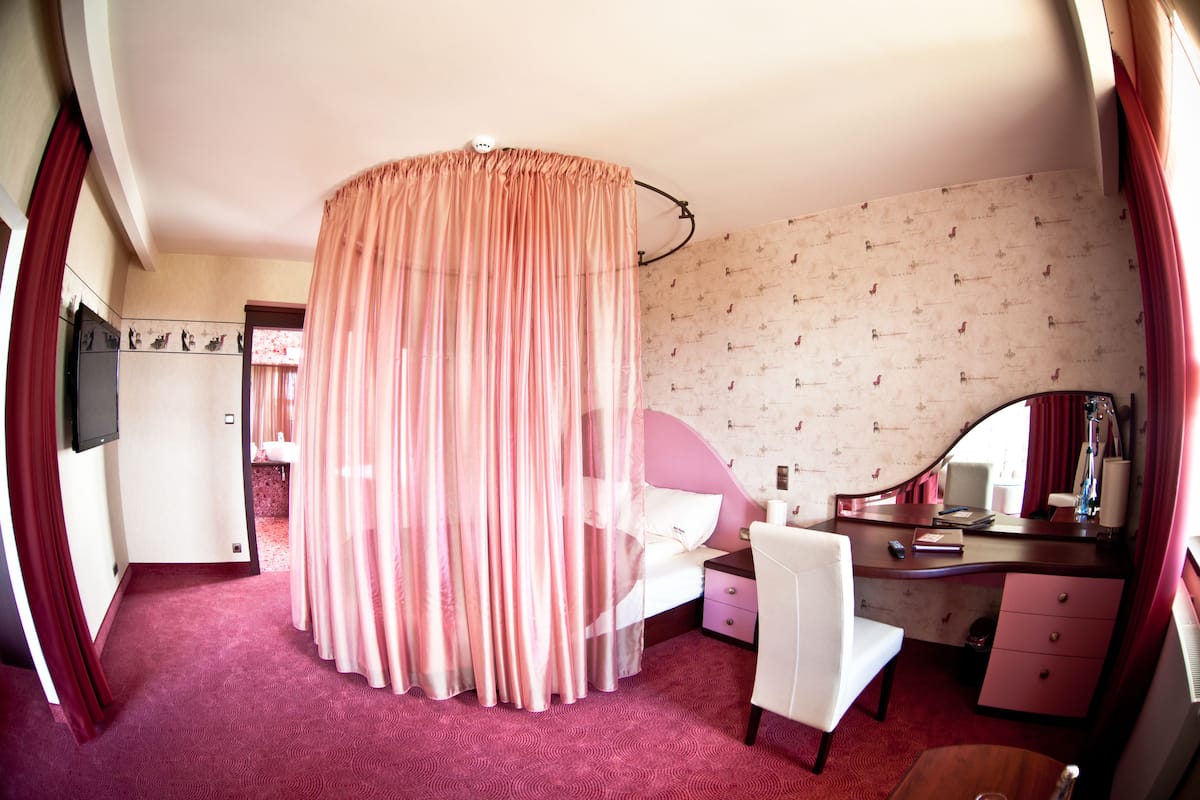 A bedroom with a bed, a desk, a chair, a vanity, and a mirror.