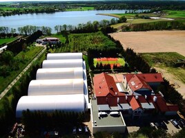 Un grand bâtiment comprenant plusieurs silos blancs, un ensemble de bâtiments à toits rouges et un lac en arrière-plan.