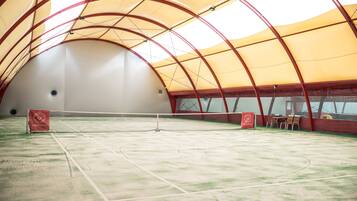 Un court de tennis intérieur équipé d’un filet, d’un auvent rouge et jaune et d’un espace pour les spectateurs.