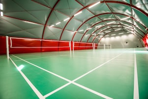 Pista de tênis coberta com superfície verde e linhas de demarcação brancas, cercada por uma rede vermelha e branca.