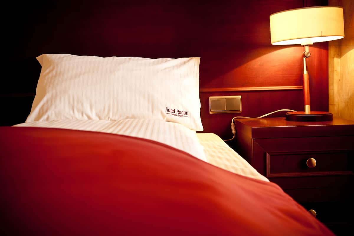 A hotel room with a neatly made bed, a bedside lamp, and a nightstand with a phone.