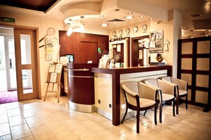 Un espace d’accueil avec un comptoir en bois, plusieurs chaises, une horloge et un tableau encadré au mur.