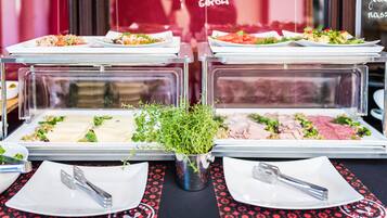Montaje de bufé con diversos platos, entre ellos ensaladas, carnes y guarniciones, presentados en recipientes transparentes.