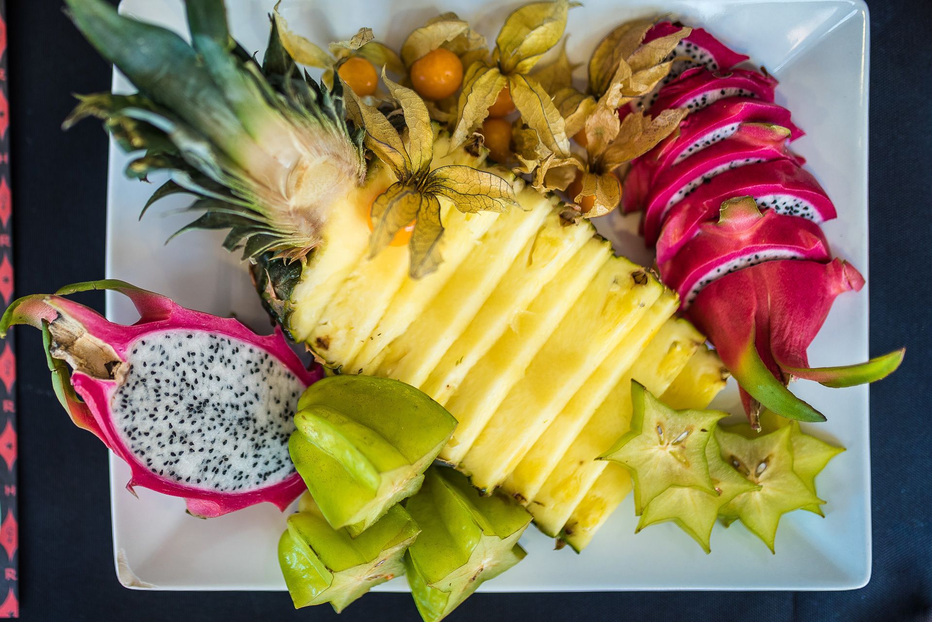 A plate with sliced dragon fruit, pineapple, star fruit, and a whole dragon fruit.