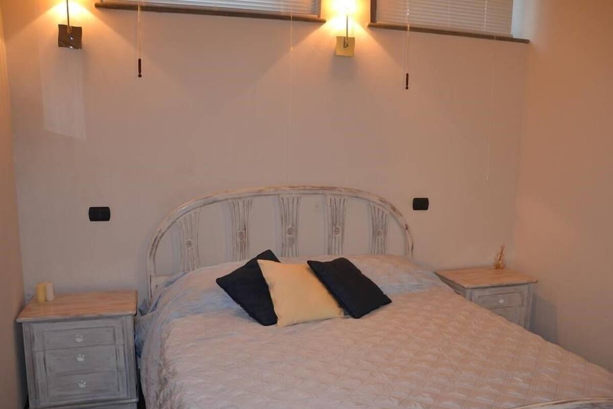 A bedroom with a bed, two bedside tables, and wall-mounted lights.